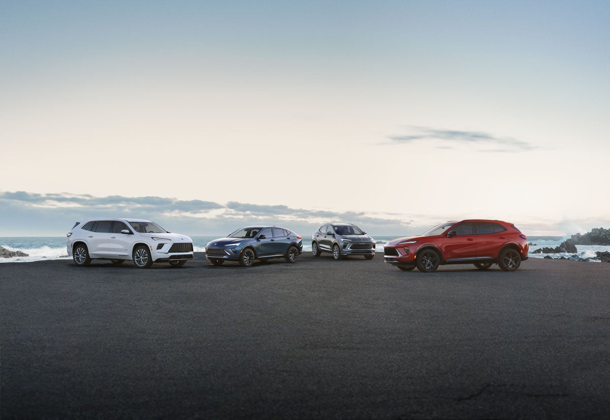 Four Buick SUVs (white, blue, gray, and red) parked on asphalt overlooking a seascape at dusk.